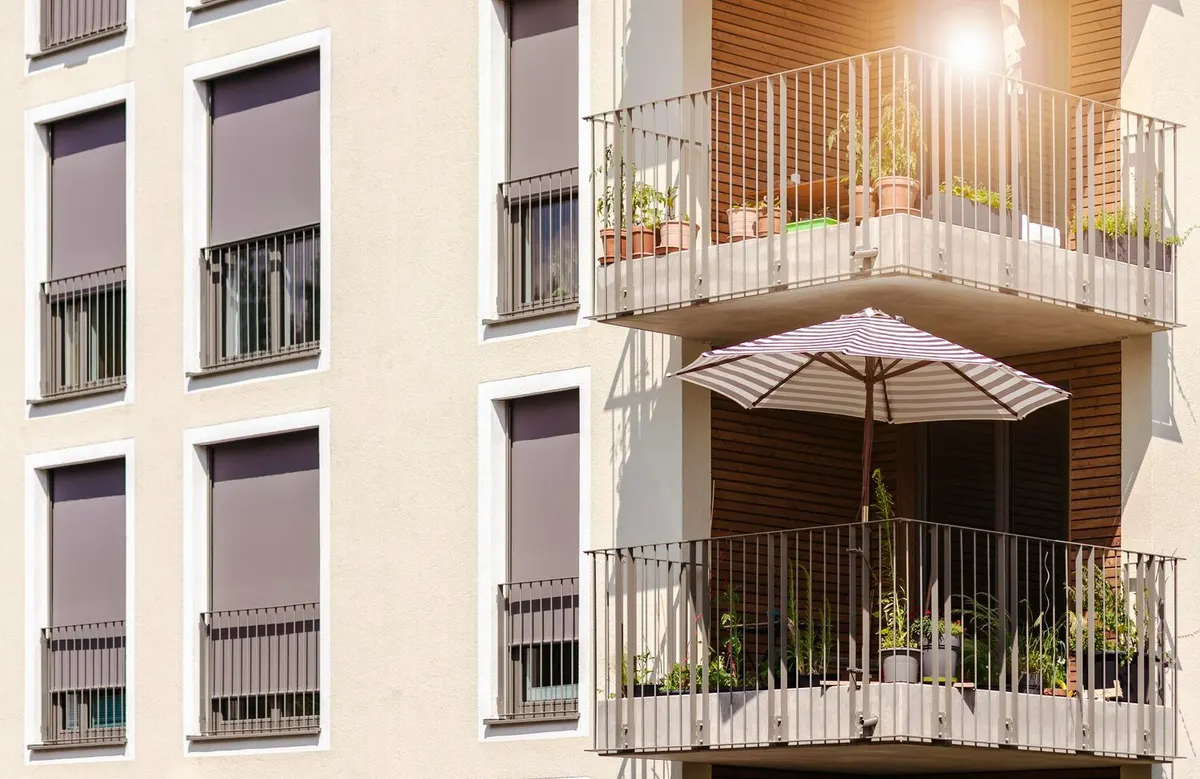Façade d'un immeuble d'habitation récent : fenêtres équipées de volets roulants extérieurs à demi baissés et balcons garnis de plantes